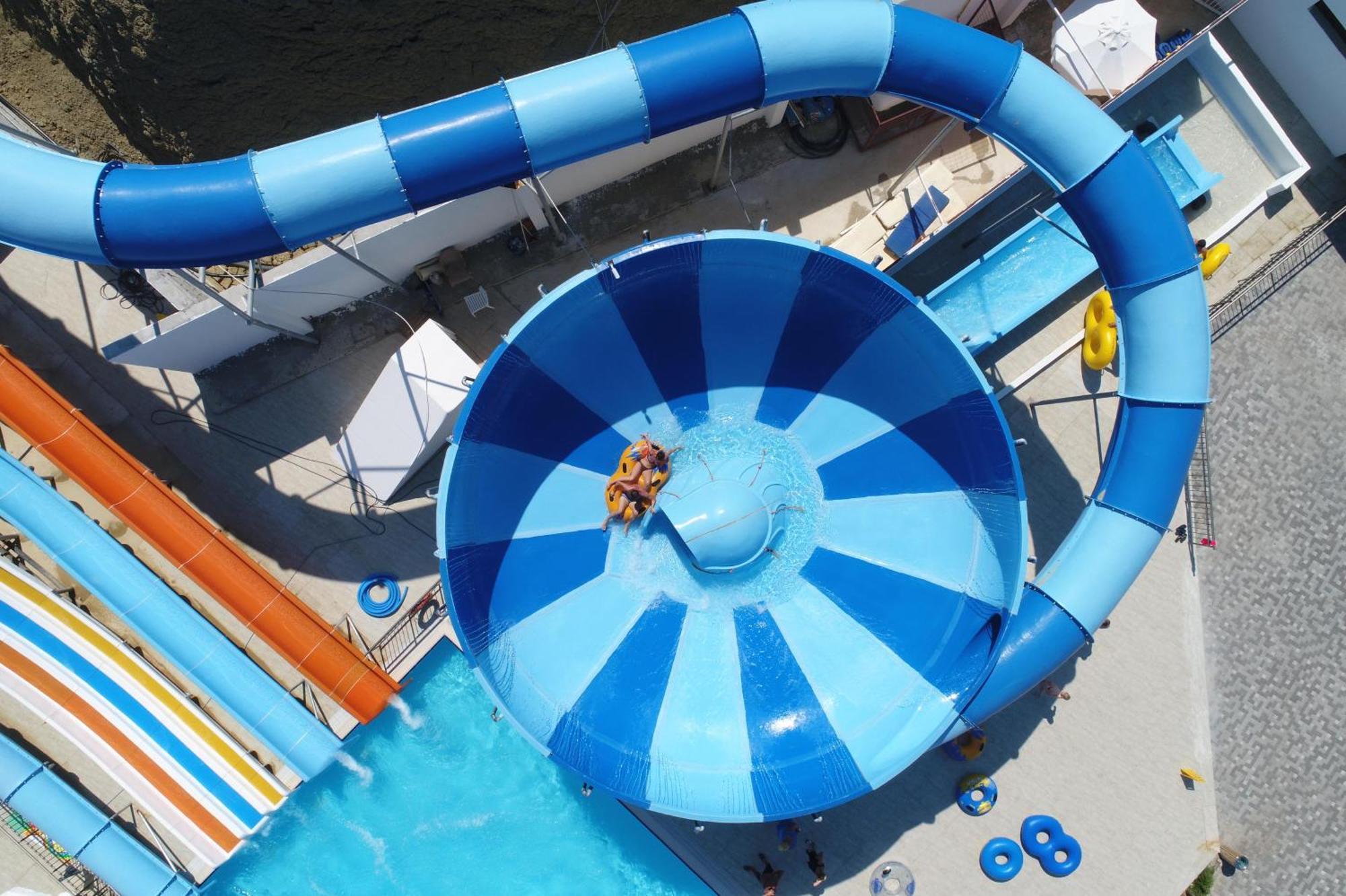 Acapulco Resort Hotel Agios Epiktitos ภายนอก รูปภาพ The photo shows a vibrant water amusement park scene from an aerial view. It features a large, circular water slide that leads into a wide funnel-shaped basin. The slide is colored blue and white, with a twisting design that adds excitement. Inside t